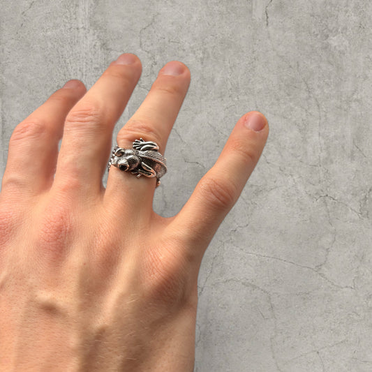 Silver stainless steel ring shaped like a detailed lizard with smiling face wrapped around finger on hand
