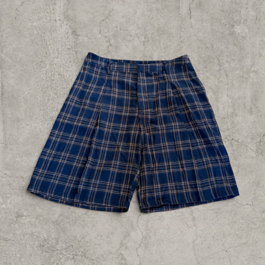 Navy blue plaid baggy pleated shorts laid flat on a concrete surface