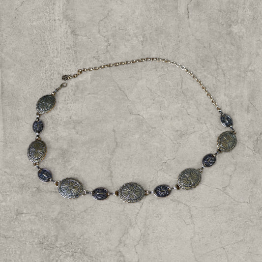 Gold metal chain belt with alternating large and small oval engraved links laid flat on a grey surface