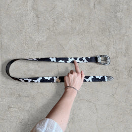 Vintage style faux leather western cowboy belt in white/black cow print with silver trim.