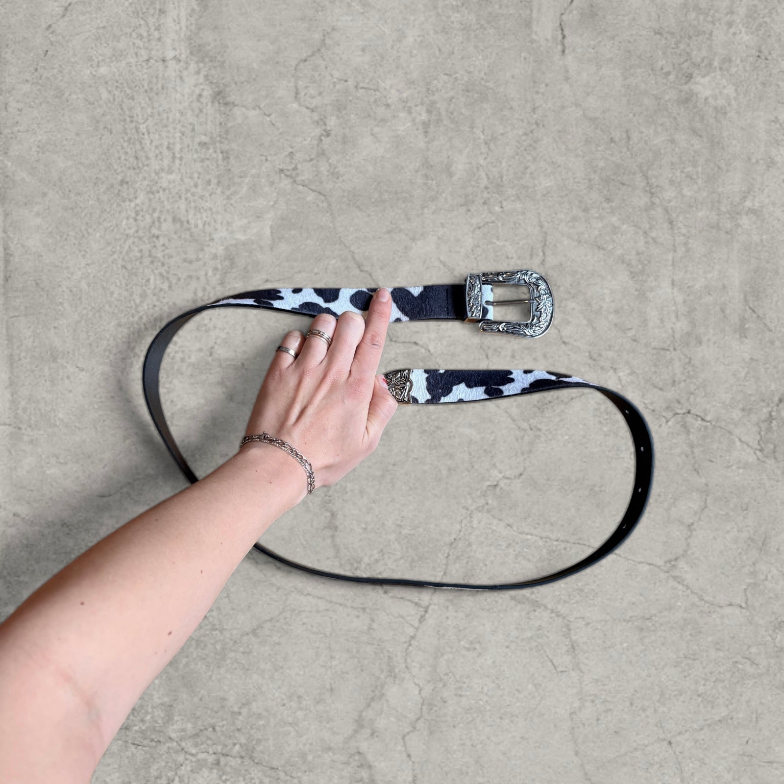 Vintage style faux leather western cowboy belt in white/black cow print with silver trim.