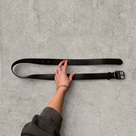 Black faux leather vintage style formal belt with grey trim and silver buckle held by hand on concrete surface