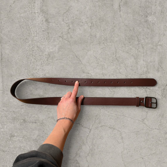 Brown faux leather formal belt with grey trim laid flat with hand pointing at adjustment holes