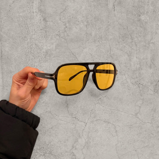 Vintage style aviator glasses with yellow tinted lenses and black frame held in hand against a concrete background