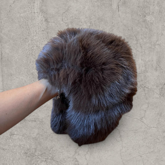Brown grey fluffy faux fur Russian Ushanka hat held by hand showing front and ear flaps