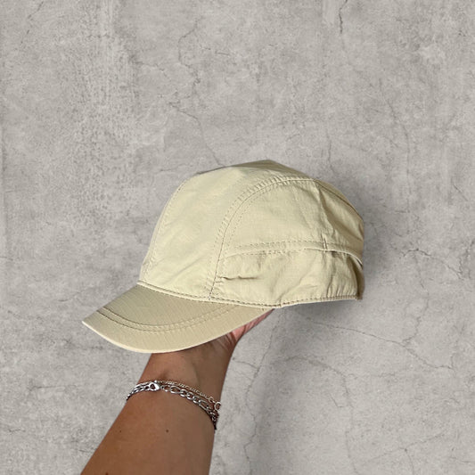 Cream vintage style hiking hat with curved brim held against a grey concrete background
