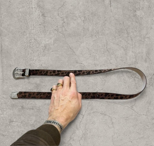 Vintage style faux leather belt in brown leopard print held by hand, laid flat on concrete surface