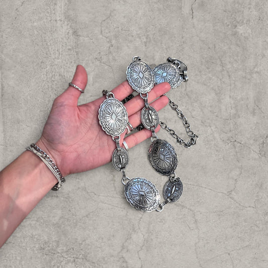 Hand holding silver vintage style western metal chain belt showing detailed oval engravings