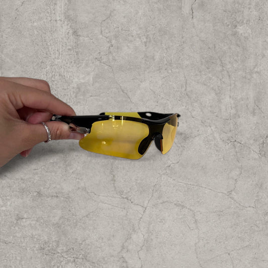 Black framed sport sunglasses held in hand showing yellow lenses and half frame design