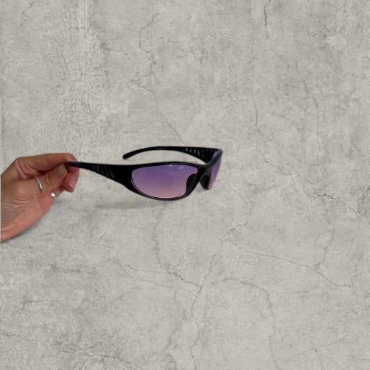 Black wraparound sunglasses with purple pink lenses and vented arms held in hand