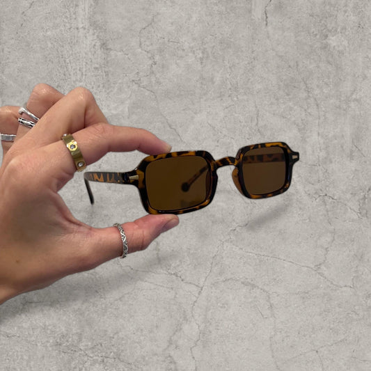 Square tinted glasses with brown lenses and black tortoise shell frame held by hand