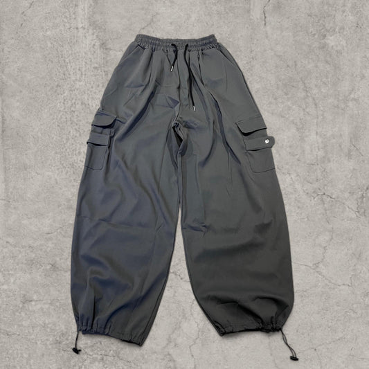 Grey baggy cargo trousers laid flat showing front with elasticated waist and drawstring