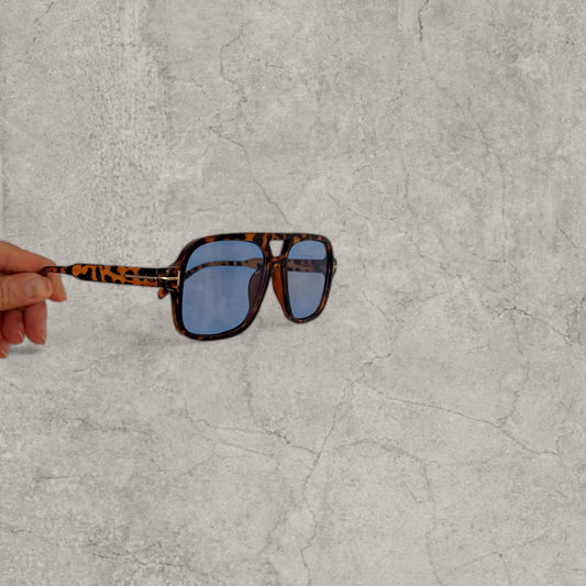 Close-up of aviator sunglasses held from the side showing brown tortoise shell frame and blue tinted lenses