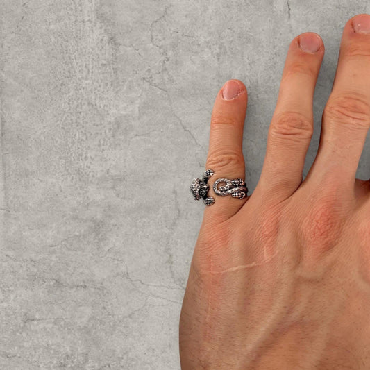 Silver stainless steel ring with monkey face worn on finger against grey textured background