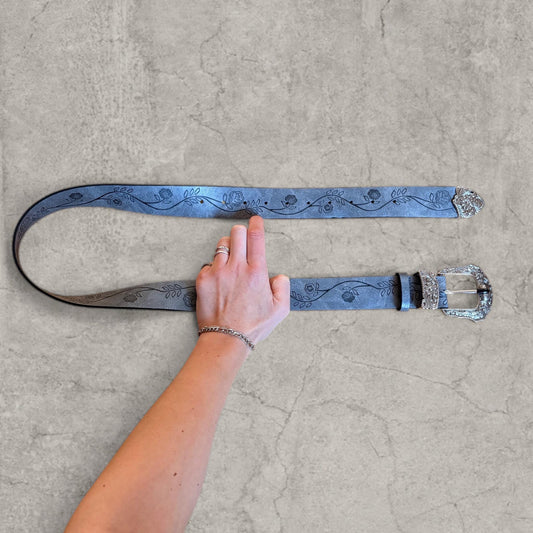Grey faux leather western cowboy belt held flat showing floral pattern and silver trimmed tip