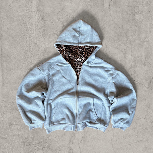 Grey baggy boxy zip-up hoodie jumper with large hood and front pocket laid flat on concrete surface