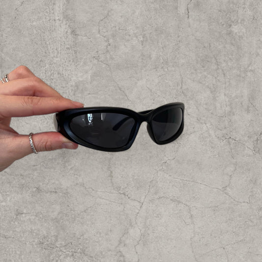 Black alien-shaped sunglasses held by hand showing front with black lenses