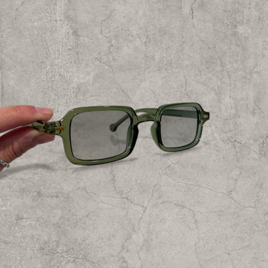 Green tinted square glasses with khaki green plastic frame held against grey concrete background