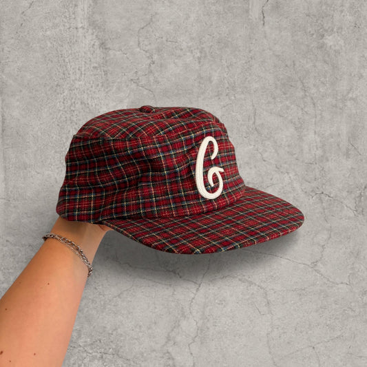 Hand holding vintage style baseball cap in red burgundy checkered plaid with white logo on front