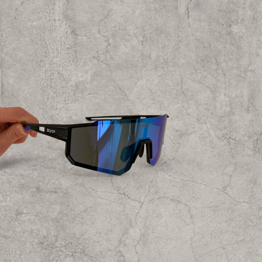 Black hard plastic sport sunglasses with wide blue purple reflective lens and cut-out arms held by hand