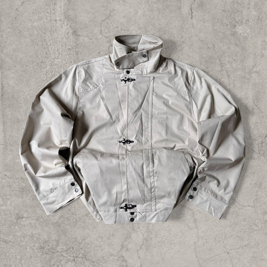 Beige cream military style bomber jacket laid flat showing front with silver clasps and high collar
