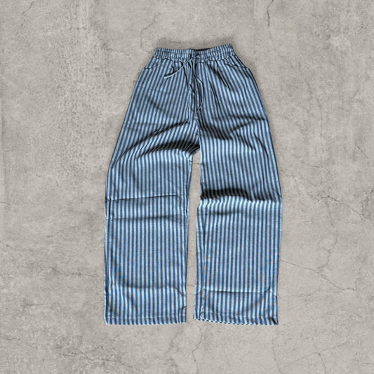 Grey and beige vertically striped wide leg trousers flat laid on concrete surface front view