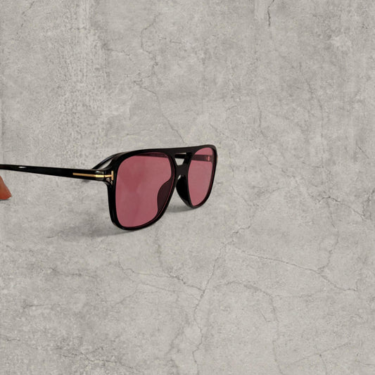 Black aviator style sunglasses with pink tinted lenses held against grey background