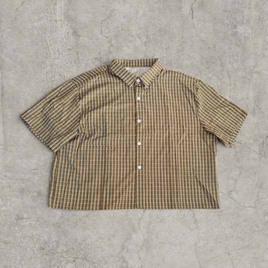 Boxy short sleeve shirt in brown and white plaid laid flat on grey surface front side showing buttons
