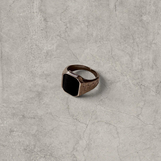 Silver colour signet ring with black square onyx gem on textured checkered band on grey surface