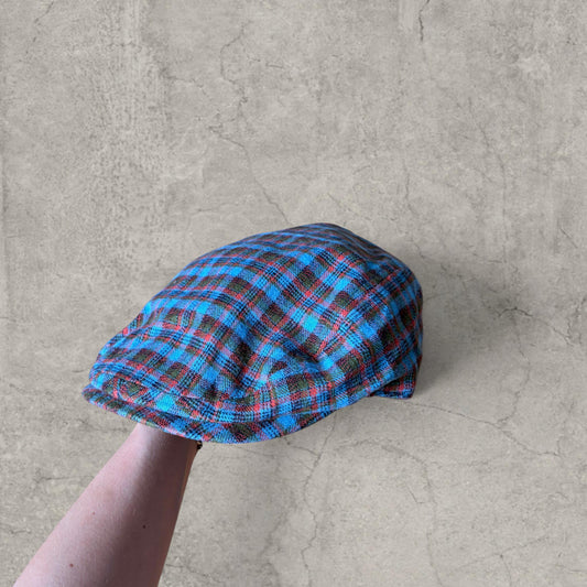Flat peak beret cap in blue checked plaid held by hand showing front and side view