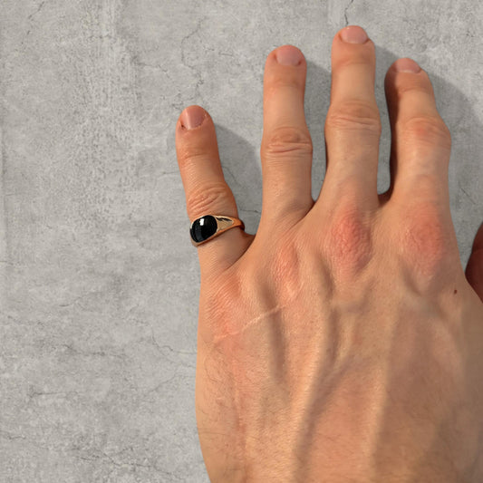 Hand wearing gold colour stainless steel signet ring with black onyx gemstone on finger