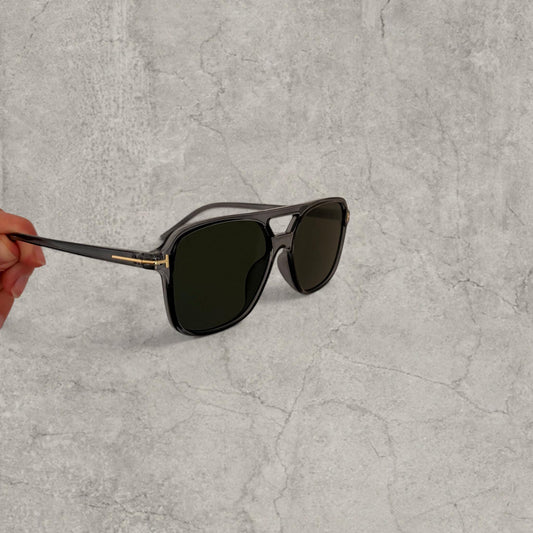 Black aviator style sunglasses with grey lenses held sideways showing thin temples and gold hinge detail