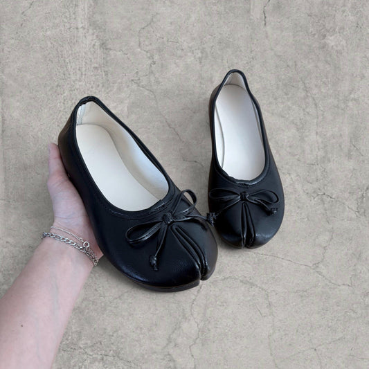 Pair of black vintage-style tabi mules held in hand showing bow and split toe detail