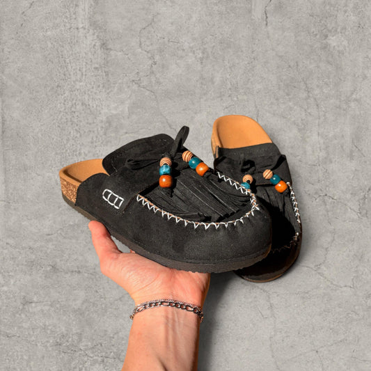 Black lace-up mule shoe with bead detailing held in hand against a grey textured background