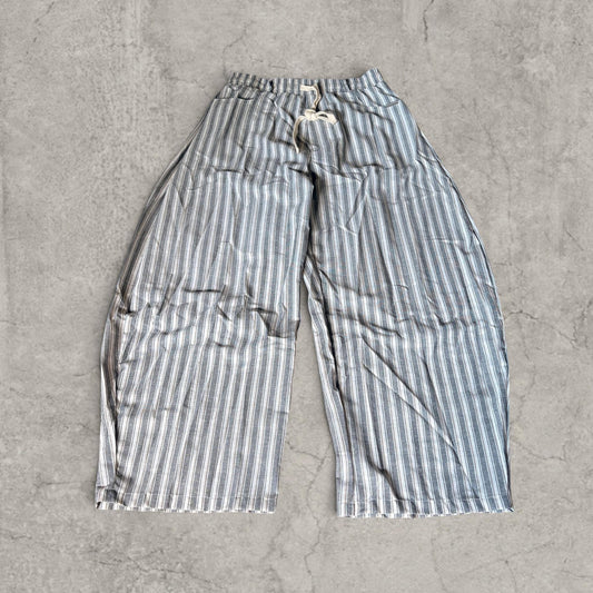 Wide-leg striped trousers laid flat on concrete with grey beige and blue pinstripes, drawstring waist and pockets
