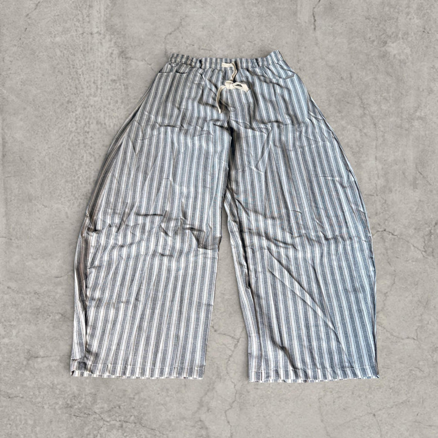 Wide-leg striped trousers laid flat on concrete with grey beige and blue pinstripes, drawstring waist and pockets