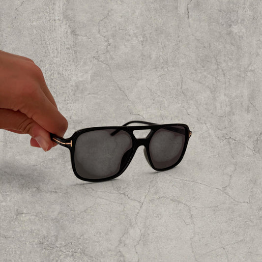 Black framed vintage aviator style sunglasses held by hand against light grey background
