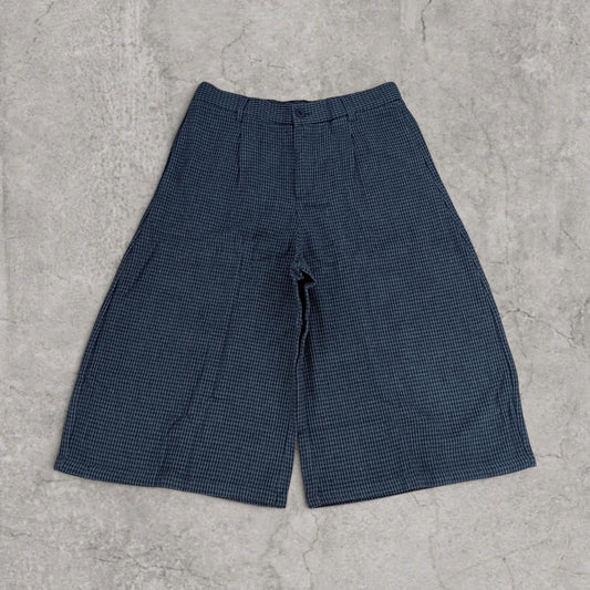 Front view of black twill baggy shorts with pleats and wide legs on a concrete surface