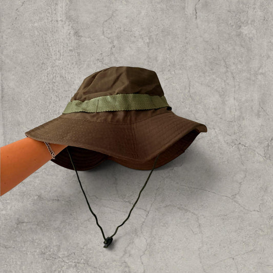 Front view of khaki green boonie jungle bucket hat with toggle chin strap held against a grey background